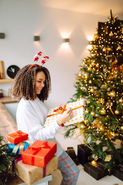 Porträt der jungen Frau in Weihnachtsmann-Hut mit Geschenk am Weihnachtsbaum Weihnachten Neujahr