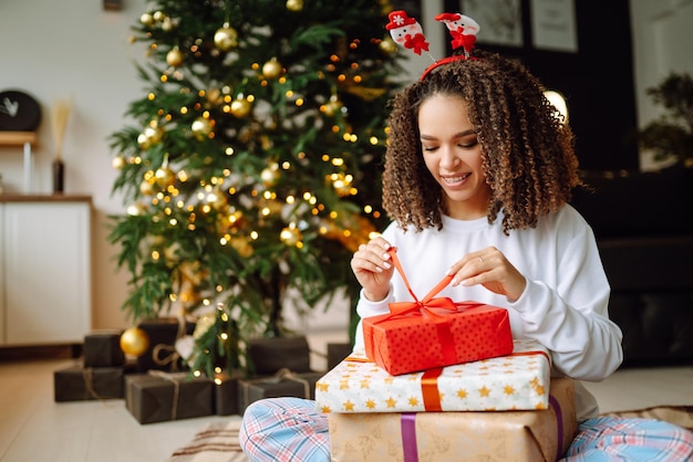 Porträt der jungen Frau in Weihnachtsmann-Hut mit Geschenk am Weihnachtsbaum Weihnachten Neujahr