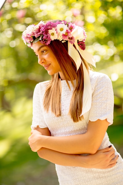 Porträt der jungen Frau mit Kranz von frischen Blumen auf Kopf im Park