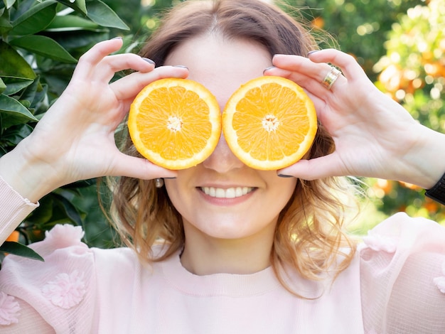 Porträt der jungen hübschen Frau, die zwei orange Hälften vor ihren Augen hält