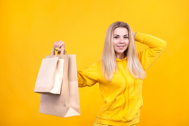 Porträt der jungen hübschen kaukasischen blonden Frau mit Papieröko-Taschen im gelben Sportanzug, lokalisiert