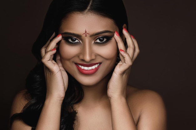 Porträt der jungen indischen Frau mit schönem Make-up und Frisur auf braunem Hintergrund