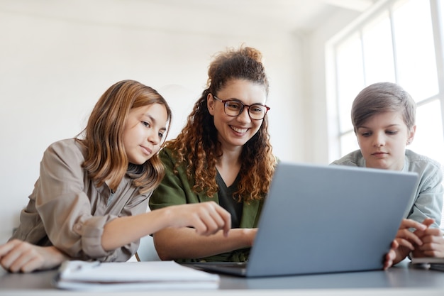 Porträt der jungen Lehrerin, die Computer mit Kindern verwendet