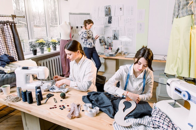 Porträt der jungen modekleidmacherinnen bei der arbeit. schneiderin, schneiderin, mode- und showroom-konzept - porträt talentierter schneiderinnen, die mit textilien zum nähen von kleidung arbeiten