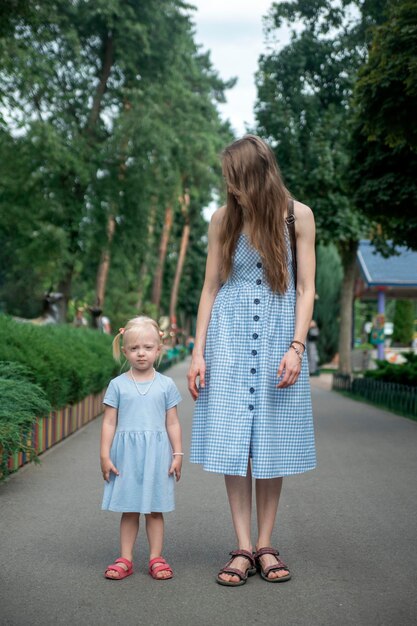 Porträt der jungen Mutter und der kleinen Tochter in blauen Kleidern, die im Park spazieren Vertikaler Rahmen