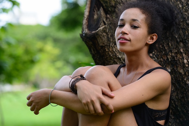 Porträt der jungen schönen afrikanischen Frau mit Afro-Haaren, die am Park draußen entspannen