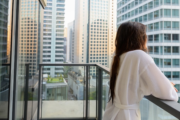 Porträt der jungen schönen asiatischen Frau, die den Blick der Stadt vom Balkon genießt