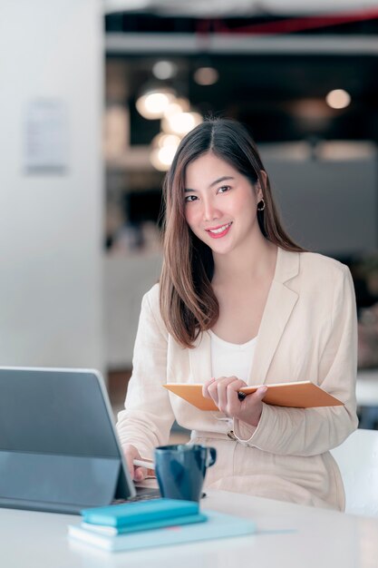 Porträt der jungen schönen asiatischen Frau, die Notizbuch hält und auf Tablette arbeitet