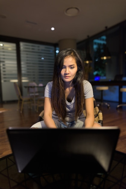 Porträt der jungen schönen asiatischen Frau unter Verwendung des Laptops im Wohnzimmer