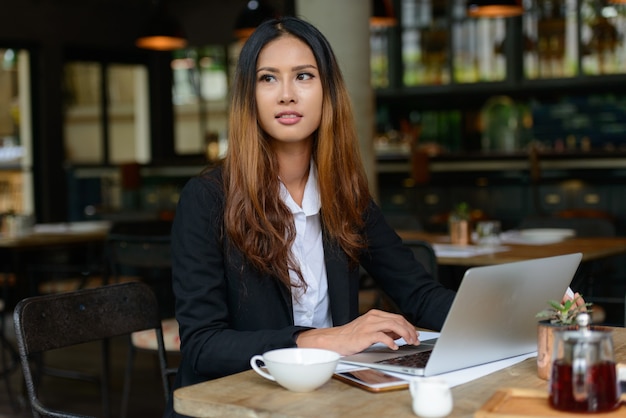 Porträt der jungen schönen asiatischen Geschäftsfrau, die am Kaffeehaus arbeitet