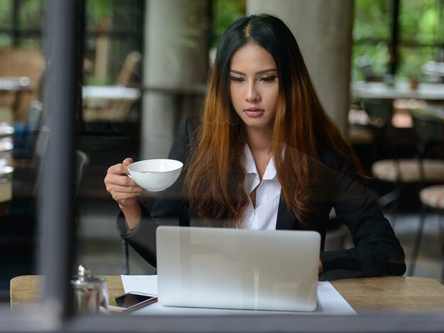 Porträt der jungen schönen asiatischen Geschäftsfrau, die am Kaffeehaus arbeitet