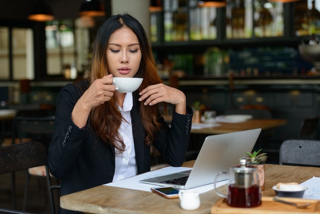 Porträt der jungen schönen asiatischen Geschäftsfrau, die am Kaffeehaus arbeitet