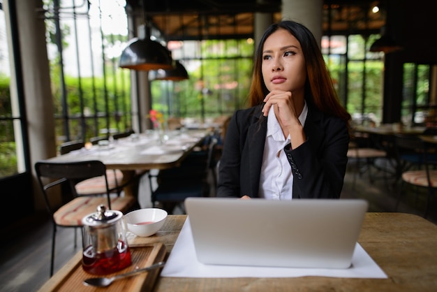 Porträt der jungen schönen asiatischen Geschäftsfrau, die am Kaffeehaus arbeitet