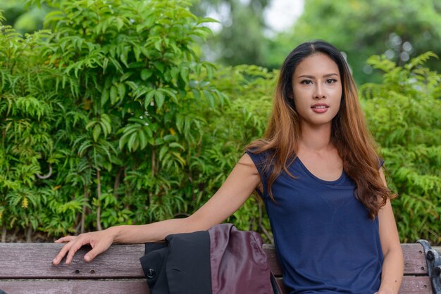 Porträt der jungen schönen asiatischen Geschäftsfrau, die am Park draußen entspannt
