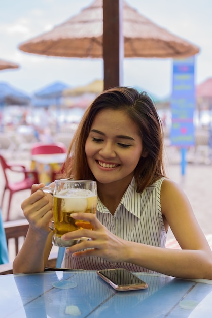 Porträt der jungen schönen asiatischen touristenfrau, die am restaurant am strand draußen sitzt