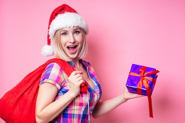 Porträt der jungen schönen blonden erstaunten Frau mit Weihnachtskastengeschenk auf rotem Hintergrund