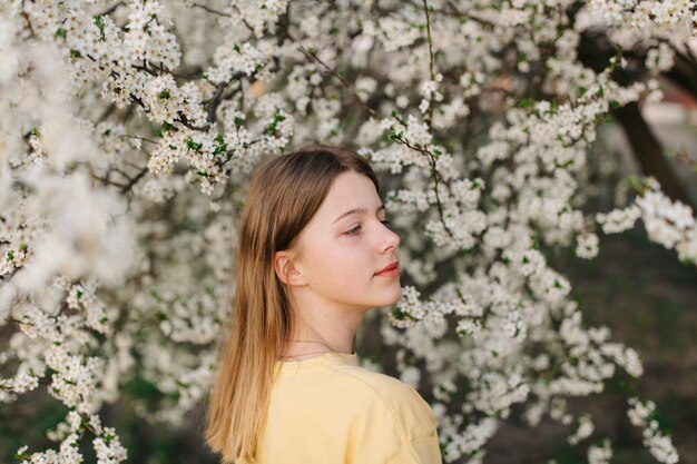 Porträt der jungen schönen blonden Frau nahe blühendem Baum mit weißen Blumen an einem sonnigen Tag.