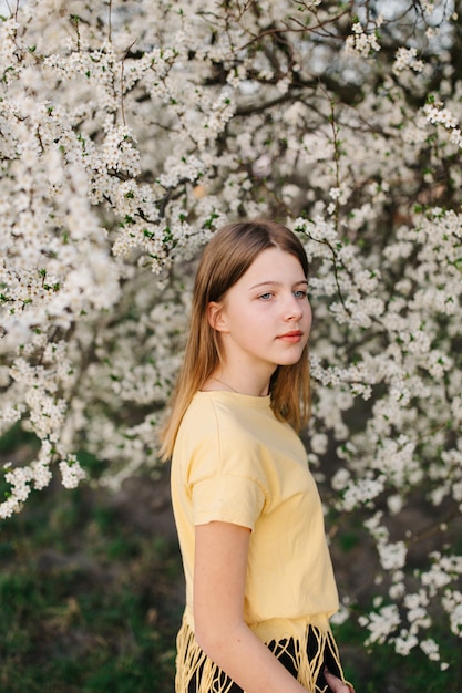 Porträt der jungen schönen blonden Frau nahe blühendem Baum mit weißen Blumen an einem sonnigen Tag.