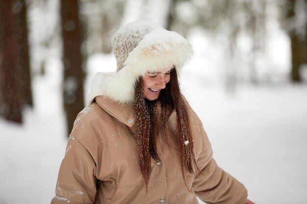 Porträt der jungen schönen Frau des glücklichen positiven Mädchens, die Spaß im verschneiten Wald an den kalten Wintertagen hat, die mit Schnee spielen, genießen Sie den frostigen Wintertag an den Winterferien, die weißen Schnee in die Luft werfen