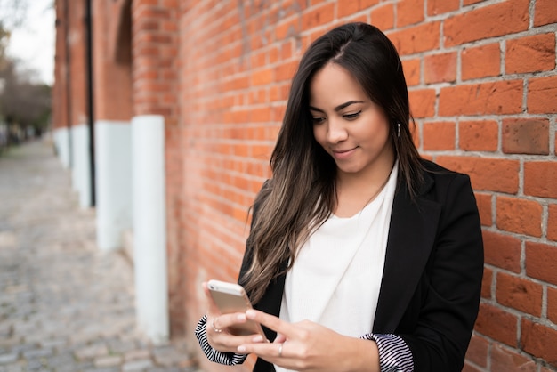 Porträt der jungen schönen Frau, die ihr Handy draußen in der Straße benutzt.