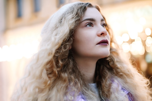 Porträt der jungen schönen Frau mit dem lockigen blonden Haar draußen. Schönheit, Modekonzept. Streetstyle. Bokeh Hintergrund