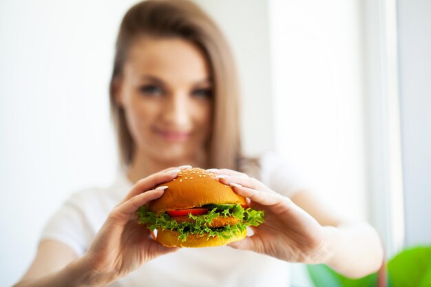 Porträt der jungen schönen hungrigen Frau, die Burger isst