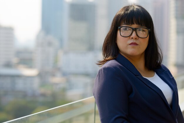 Porträt der jungen schönen übergewichtigen asiatischen Geschäftsfrau gegen Ansicht der Stadt