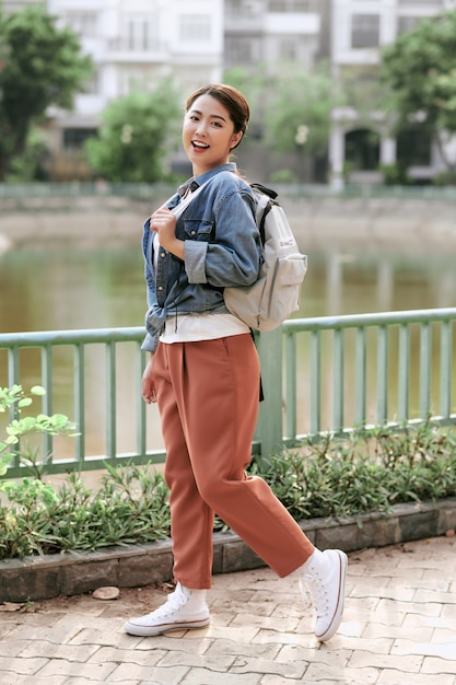 Porträt der jungen stilvollen Hipster-Frau, die auf der Straße geht, trendiges Outfit trägt, mit Rucksack reist.