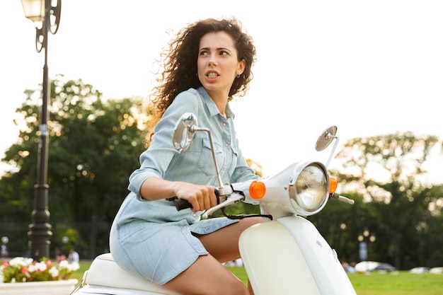 Porträt der kaukasischen Frau, die auf stilvollem Motorrad durch Stadtstraße reitet