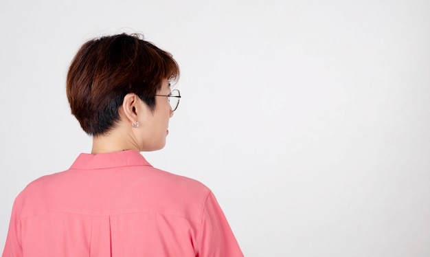 Porträt der kurzhaarigen asiatischen Frau, die ein rosa Hemd trägt, das seitlich auf Weiß lächelt