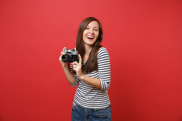 Porträt der lachenden jungen Frau in der zufälligen gestreiften Kleidung, die Retro- Weinlesefotokamera lokalisiert auf hellem rotem Wandhintergrund hält. Menschen aufrichtige Emotionen, Lifestyle-Konzept. Kopieren Sie Platz.