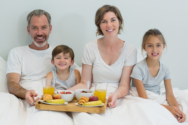 Porträt der lächelnden Familie, die Frühstück auf Bett im Schlafzimmer hat