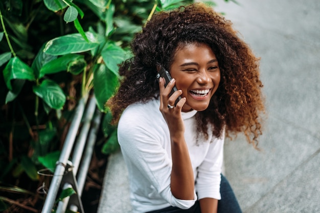 Porträt der lächelnden Frau des gelockten Haares, die am Telefon spricht.