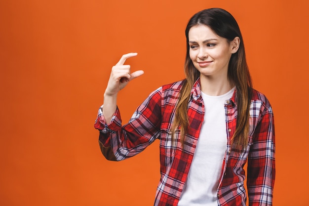 Porträt der lächelnden Frau, die kleine Menge von etwas zeigt, lokalisiert gegen orange Hintergrund.