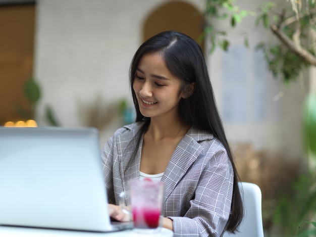 Porträt der lächelnden Geschäftsfrau, die mit Laptop auf Couchtisch im Garten der Vorderseite des Cafés arbeitet