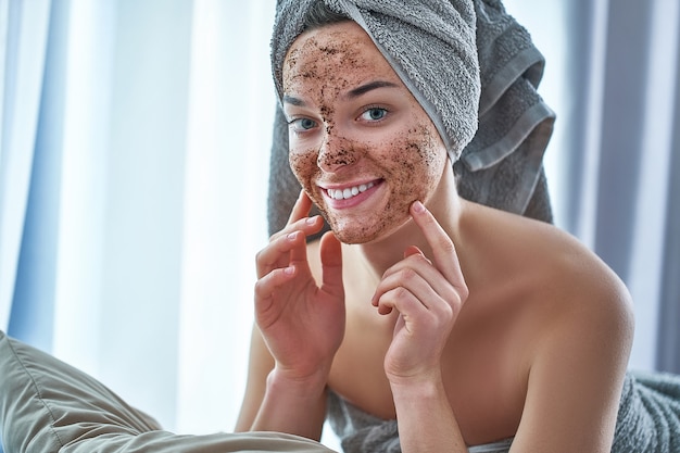 Porträt der lächelnden glücklichen Frau im Badetuch mit natürlicher Gesichtskaffee-Peelingmaske nach Dusche