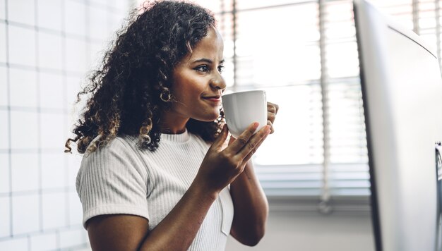 Porträt der lächelnden glücklichen schwarzen Afroamerikaner-Frau, die unter Verwendung der Technologie des Desktop-Computers beim Sitzen auf Tisch entspannt.