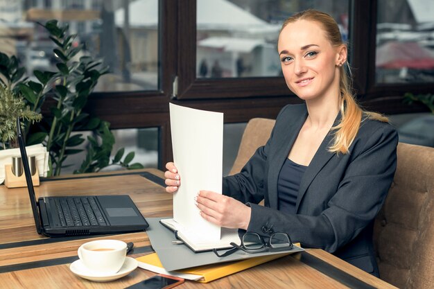 Porträt der lächelnden hübschen jungen Geschäftsfrau, die im Büro sitzt.