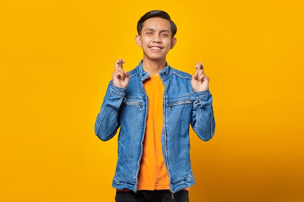 Porträt der lächelnden jungen asiatischen mannuniform, die mit dem finger auf gelbem hintergrund gekreuzt gestikuliert