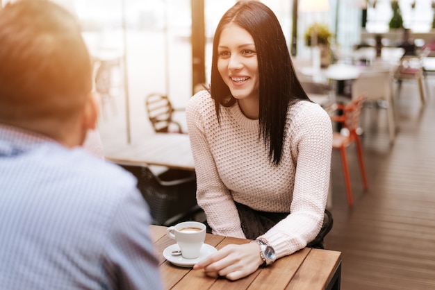 Porträt der lächelnden jungen Frau an einem Cafétisch sprechend mit Freund.