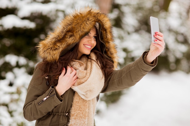 Porträt der lächelnden jungen Frau, die selfie mit Handy im Winter im Freien nimmt