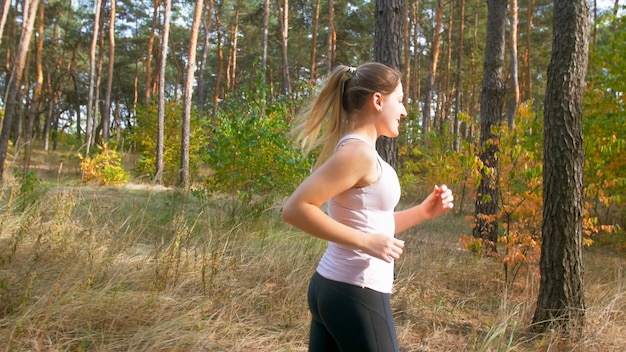 Porträt der lächelnden jungen Frau mit dem Pferdeschwanz, der im Wald läuft.