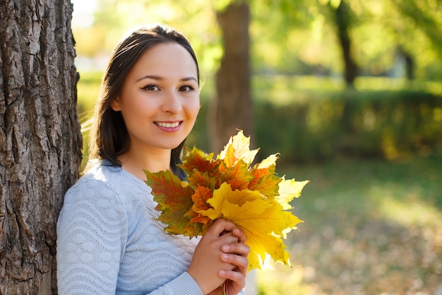 Porträt der lächelnden jungen Frau mit Herbstlaub