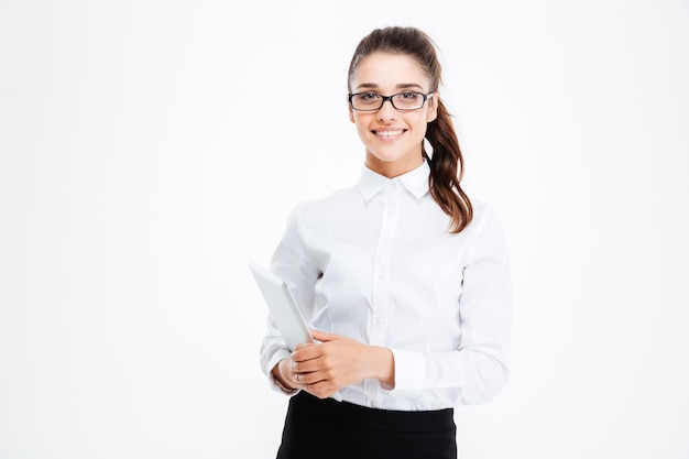 Porträt der lächelnden jungen Geschäftsfrau in den Gläsern, die Tablette über weißer Wand stehen und halten