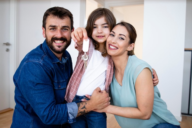 Porträt der lächelnden kaukasischen Familie, die in ihr neues Haus umzieht, während Tochter Schlüssel hält.