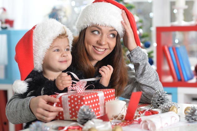 Porträt der lächelnden Mutter und der süßen kleinen Tochter, die Weihnachten zu Hause mit Weihnachtsmützen feiert