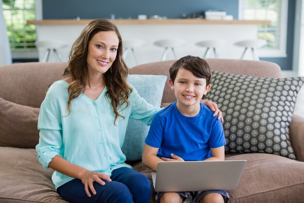 Porträt der lächelnden Mutter und des Sohnes, die auf Sofa unter Verwendung des Laptops sitzen