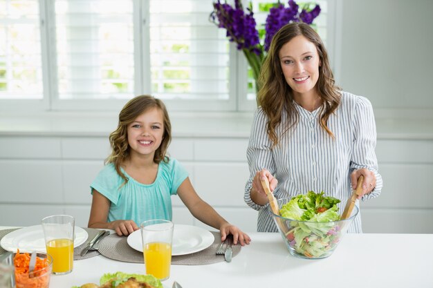 Porträt der lächelnden Mutter und Tochter, die Schüssel Salat in der Küche mischen