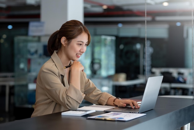 Porträt der lächelnden schönen asiatischen Geschäftsfrau genießen Sie die Idee, mit Laptop-Computer im Büro zu sitzen