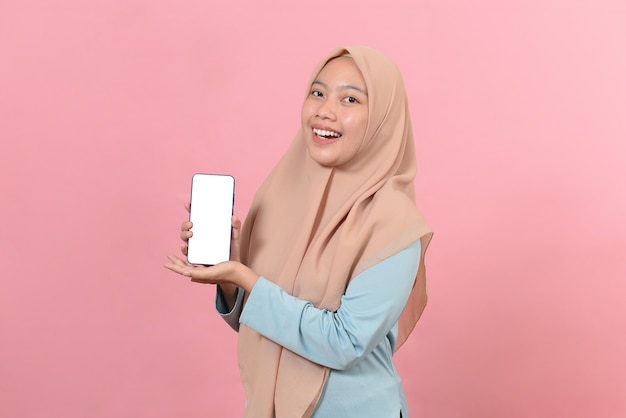 Porträt der lächelnden schönen asiatischen muslimischen Frau, die weißen Bildschirm auf dem Telefon zeigt